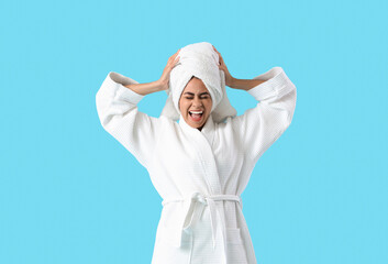 Young African-American woman in bathrobe after shower shouting on blue background