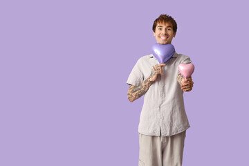 Handsome young man with air balloons in shape of heart on lilac background. Valentine's Day celebration