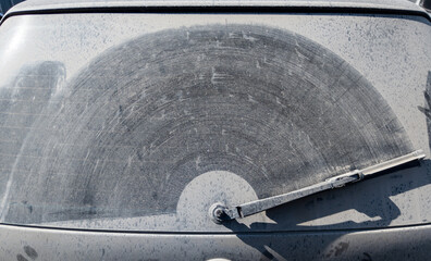dusty rear window of the car with wiper trace on layer of dirt on it