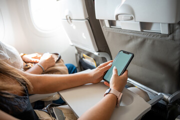 Hands of anonymous woman using her phone while flying in an airplane. Unrecognizable person...