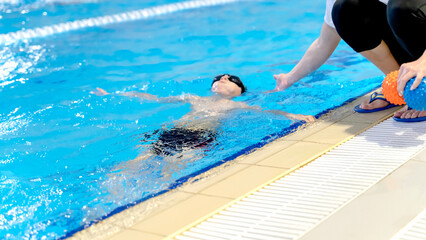 A boy learns to swim with a coach in the pool