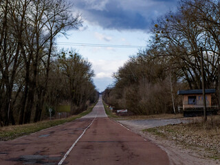 A red road with a white line down the middle in a rural area. Long straight road to the Chernobyl radioactive exclusion zone.