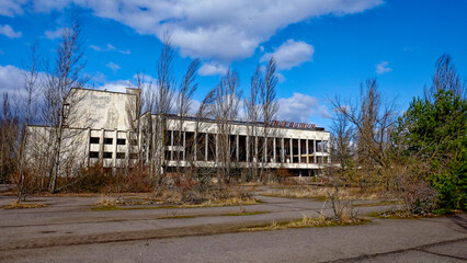 Fototapeta na wymiar A dilapidated building with broken windows, surrounded by overgrown vegetation and bare trees. The Energetik Palace of Culture is a now abandoned multifunctional palace of culture in Pripyat.