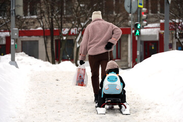 Woman rides a child on sledge, family leisure in winter city