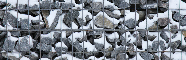 Snowy gabion, texture, background. Fragment of gabion net (design), filled with snow. New technologies in the manufacture of retaining walls and fences. Landscaping. Gabion, covered with snow. Winter