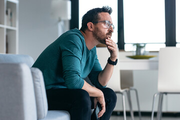 Worried mature man thinking about what he has read on his mobile phone while sitting on the couch...