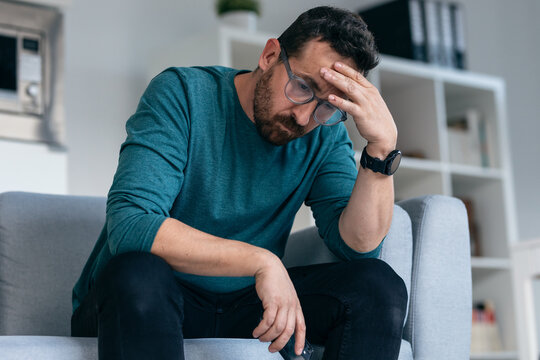 Worried mature man thinking about what he has read on his mobile phone while sitting on the couch at home