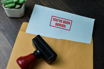 Concept of You've Been Served text on Document above brown envelope isolated on Wooden Table.
