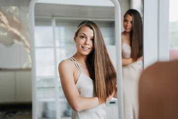 Young woman in a light dress smiling confidently at the camera, reflected in a mirror in a...