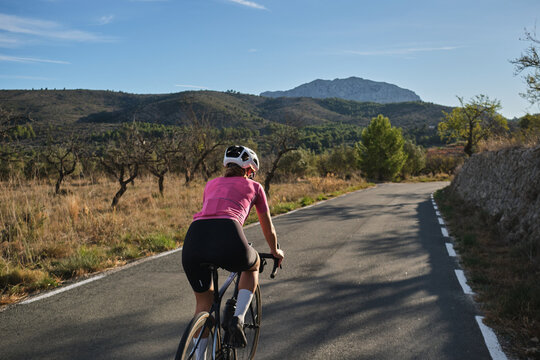 Fit female cyclist riding a gravel bike with a view of the Spanish mountains. Athlete wearing sportswear and helmet. Sports motivation image. Good road for cycling. Mountain Bernia, Alicante, Spain.