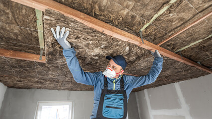 Ceiling insulation. The Worker putting a thermal insulation from glass wool. - obrazy, fototapety, plakaty