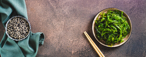 Delicious wakame seaweed salad on a plate and sesame seeds in a bowl top view web banner