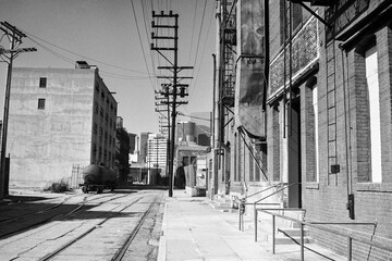Grainy archival 1985 black and white film photograph of Banning Street near Santa Fe Ave in downtown Los Angeles California.  The brick warehouses have been torn down.