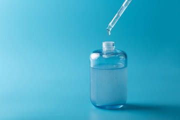 Serum pipette in close-up with a falling drop on a blue background, cosmetic packaging with a...