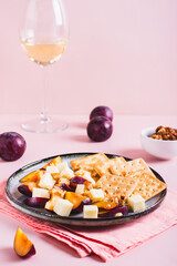 Dinner for girls, cheese, biscuits, plums on a plate and a glass of wine on the table vertical view