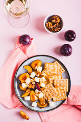 Dinner for girls, biscuits, cheese, plums and walnuts on a plate on pink top and vertical view