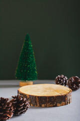Podium made from a cut tree trunk, Christmas tree and pine cones on a green vertical view