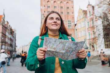 Portrait beautiful woman with paper map in street. Happy tourist travels in Europe. Vacation concept by exploring interesting places to travel. Women Searching locations at autumn day. Gdansk, Poland