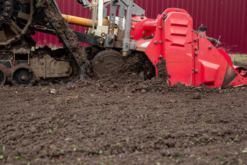 caterpillar tractor with a tillage cutter loosens the soil in a garden plot.