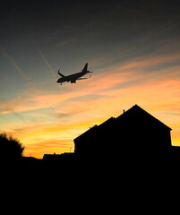 Silhouette of a passenger plane flying low over houses at dawn as it approaches an airport to land....