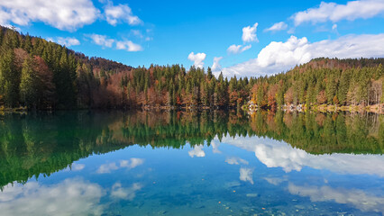 Panoramic view of Fusine Lake (Laghi di Fusine) in Tarvisio, Friuli-Venezia Giulia, Italy, Europe. Water reflection in clear green alpine lake. Autumn colored foliage. Calm serene tranquil atmosphere