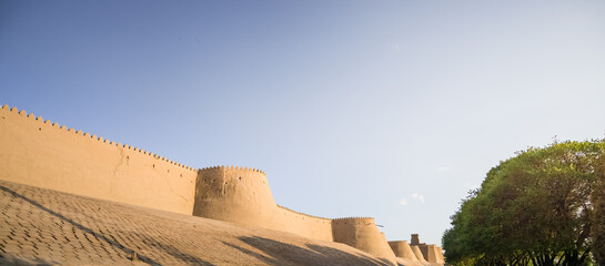 Tall ancient defensive fortifications made of bricks, clay and straw in the ancient fort city of Khiva in Khorezm, medieval architecture of the fortress at sunset