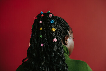 Close-up rear view of African woman with braided hair and colorful clips standing on red background