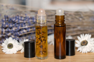 Two liquid cosmetics in roll on transparent and amber glass bottle at wooden background with white...