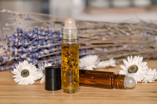 Two liquid cosmetics in roll on transparent and amber glass bottle at wooden background with white flowers and dry lavender bunch.