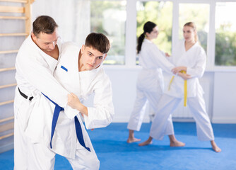 Two men practice grabbing and throwing on sports mats during judo training