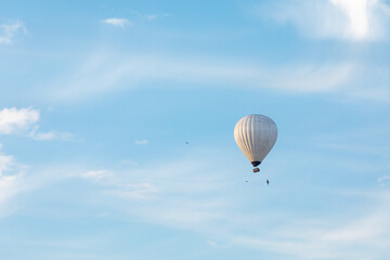 Nicely white hot-air balloon in the distance. Shot against the blue sky with thin clouds and flying birds