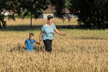 Happy child and mother are playing in field of ripening wheat. Little boy and mom travel on field. Kid and parent play in nature.