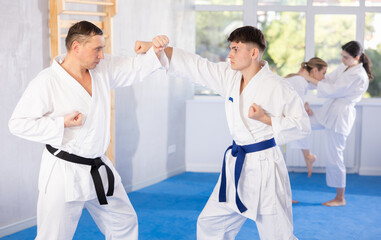 Obraz premium Sportive young guy in kimono applying attack methods on his partner during karate courses