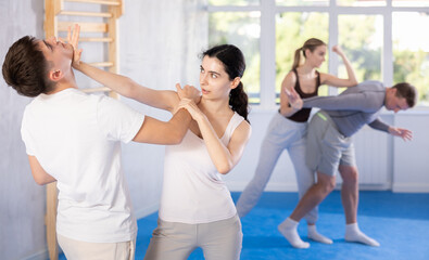 Irate young female attendee of self-defense classes fighting with male opponent in sports hall