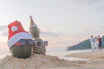 Santa Claus pineapple and watermelon couple wearing stylish sunglasses on the sand contrasting with the sea. wearing a christmas hat Christmas and New Year holiday ideas on the beach, Patong, Phuket