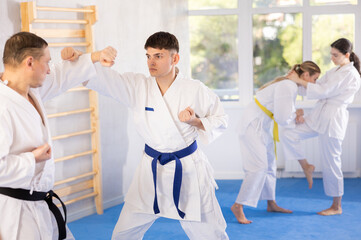 Active young male attendee of karate classes fighting with middle-aged man during workout session
