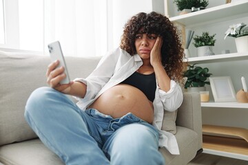 Pregnant woman blogger sits on the couch at home and takes pictures of herself on the phone, selfie...