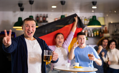 Group of young adult sports fans rooting for favorite team and waving flag of Germany while...