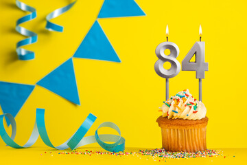 Lighted birthday candle number 84 - Yellow background with blue pennants