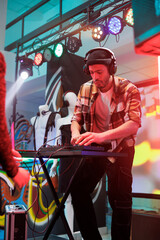 Performer playing techno music at discotheque in nightclub. Young man dj in headphones using digital controller for mixing sound on stage with spotlights at party in club