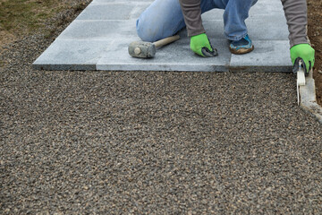 craftsman measures curbstone with folding rule while busy laying stone slabs for the walkway