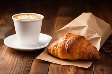 Fotobehang White cup of coffee and croissant in paper bag on wooden background © Olivia