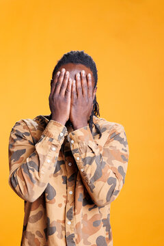 Male person doing three wise monkeys gesture on camera, covering eyes, mouth and ears as wisdom sayings. African american man advertising silence concept with hand in studio over background