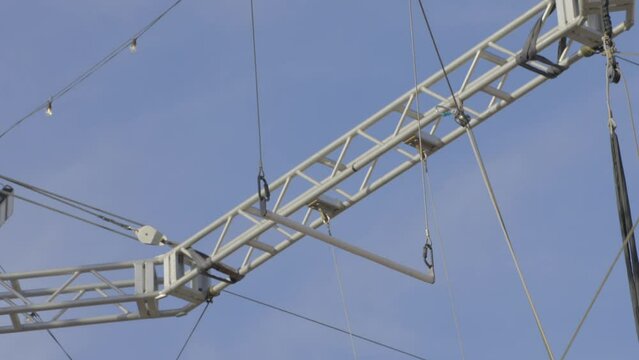 This video shows a close up view of an empty trapeze bar swinging back and forth with a blue sky in the background. 