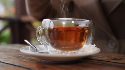 Woman adds sugar to black tea into clear cup at table in cafe. Relaxed woman sweetening tea in cafe...