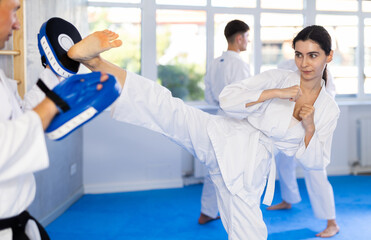 Obraz premium Young woman karateka in kimono trains kicks in studio..