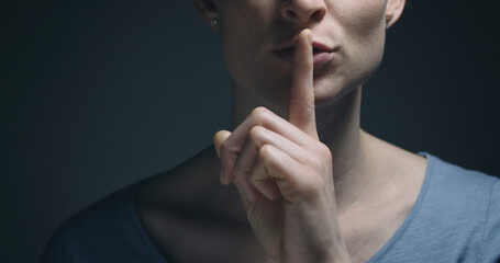 Woman gesturing to be quiet with a finger before her mouth. - 694578068
