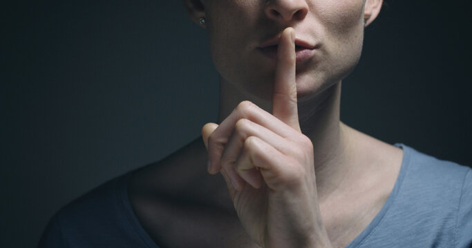 Woman gesturing to be quiet with a finger before her mouth.