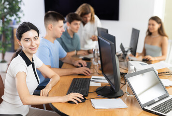 Fototapeta premium Enthusiastic young girl studying in computer lab with fellow students engrossed in coursework. Digital education concept..