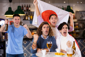 Group of happy fans celebrate victory of their favorite team with flag of Japan in a beer bar
